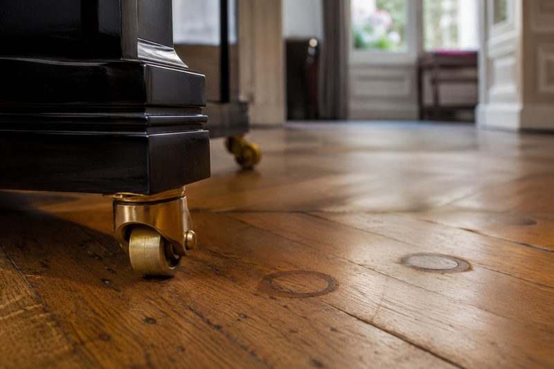 Roulettes en laiton d’un piano droit sur un parquet ancien